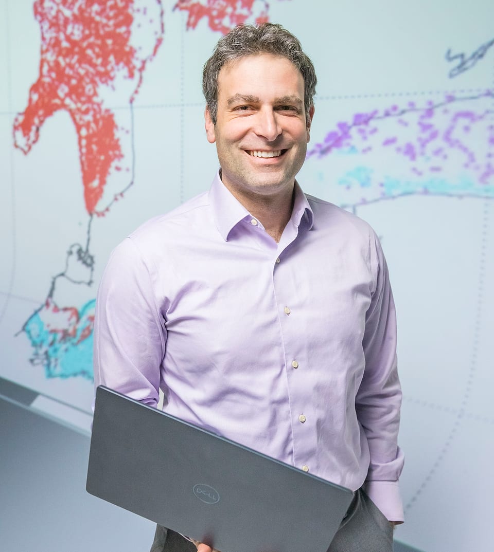Matthew J. Hoffman, Professor in the School of Mathematics and Statistics at Rochester Institute of Technology, standing in front of a world map showing plastic pollution data